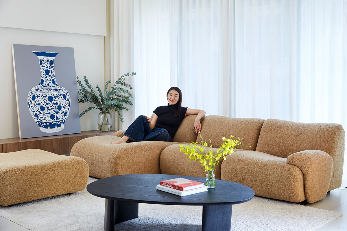 Woman sitting on a tan modular sofa in a bright living room with a black coffee table and vase artwork.